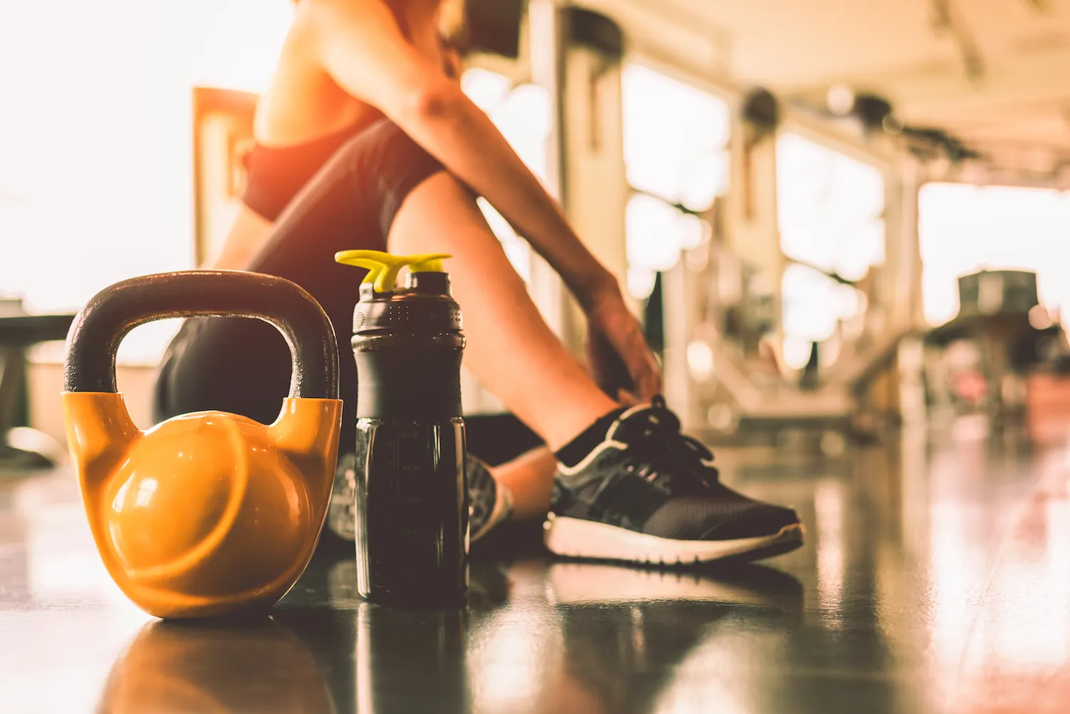 Woman resting at a gym beside a kettlebell and water bottle