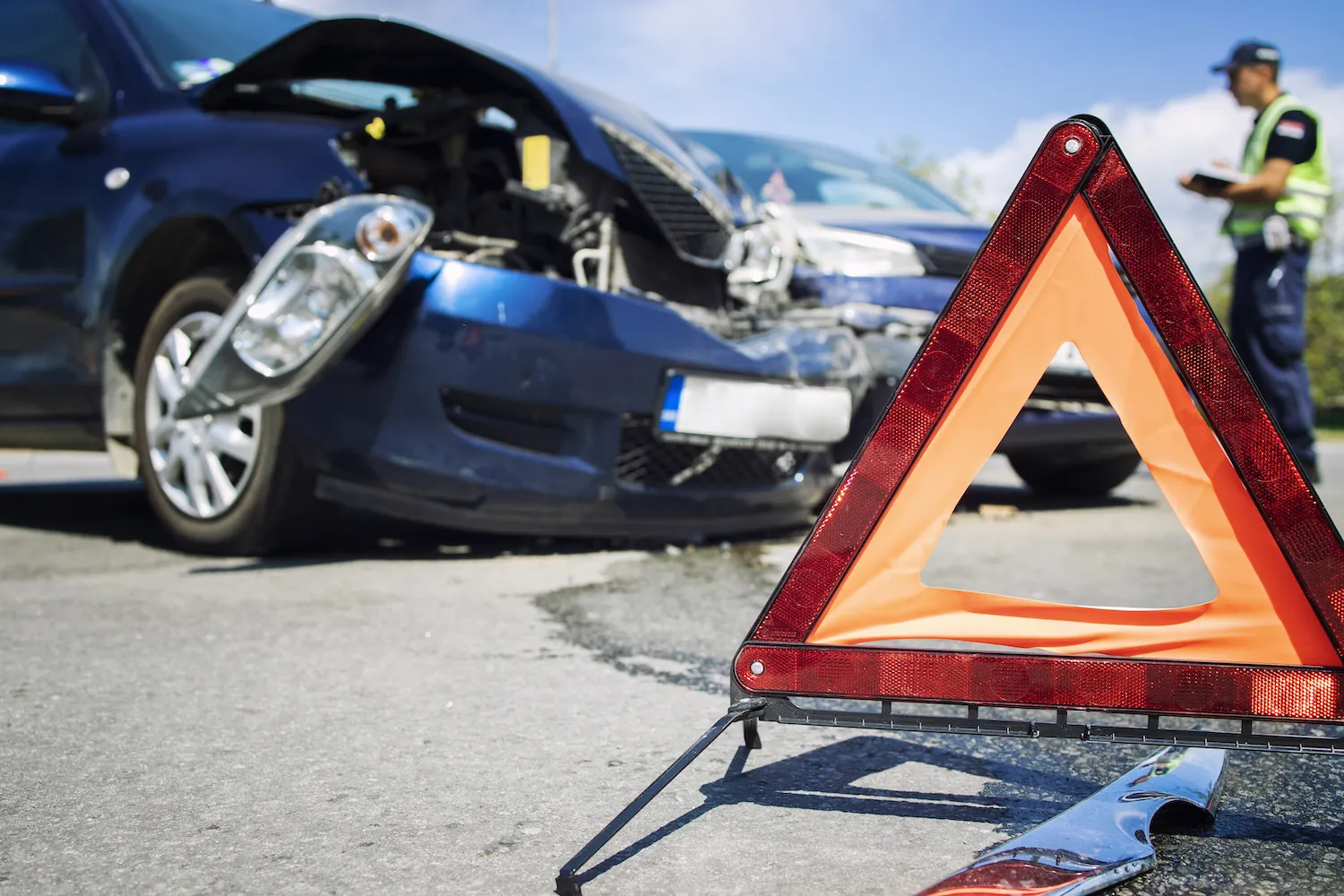 Damaged car on road with warning triangle and officer