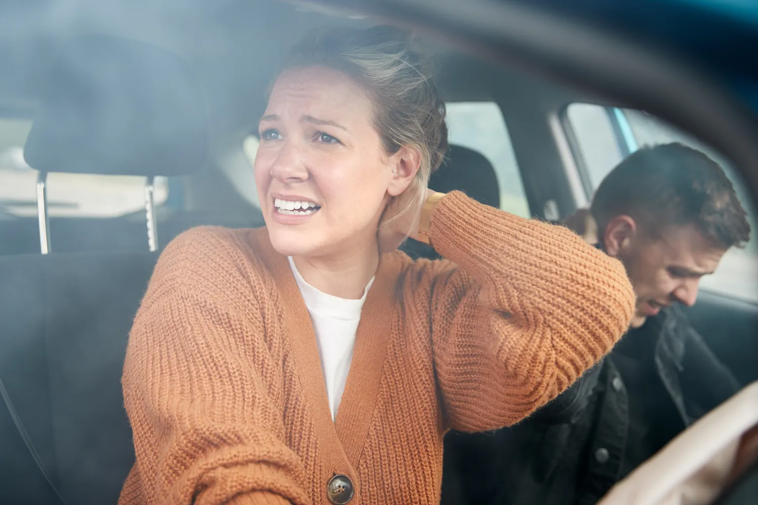 Woman in a car holding her neck, with a man slumped beside her