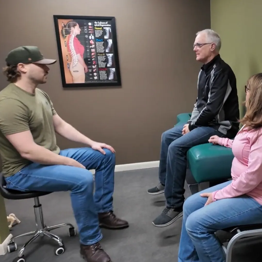 Chiropractor consulting with two patients in a room with a spine poster