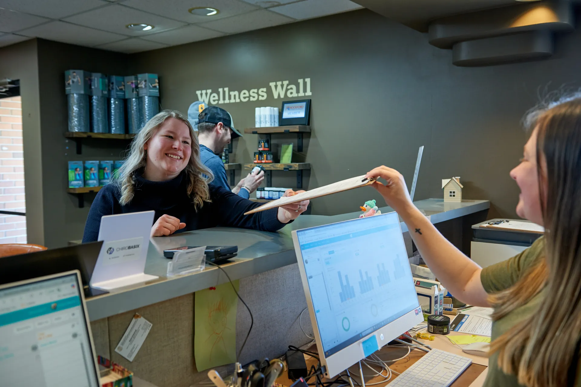 Front desk staff greeting patients by the wellness wall
