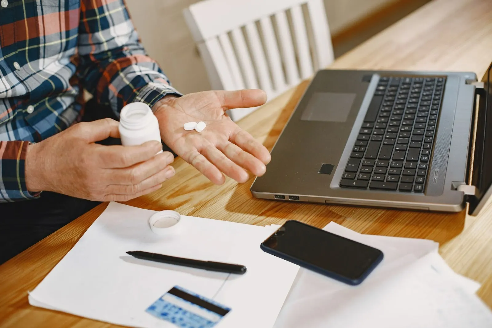 Man shaking pills from a bottle into his hand at a desk