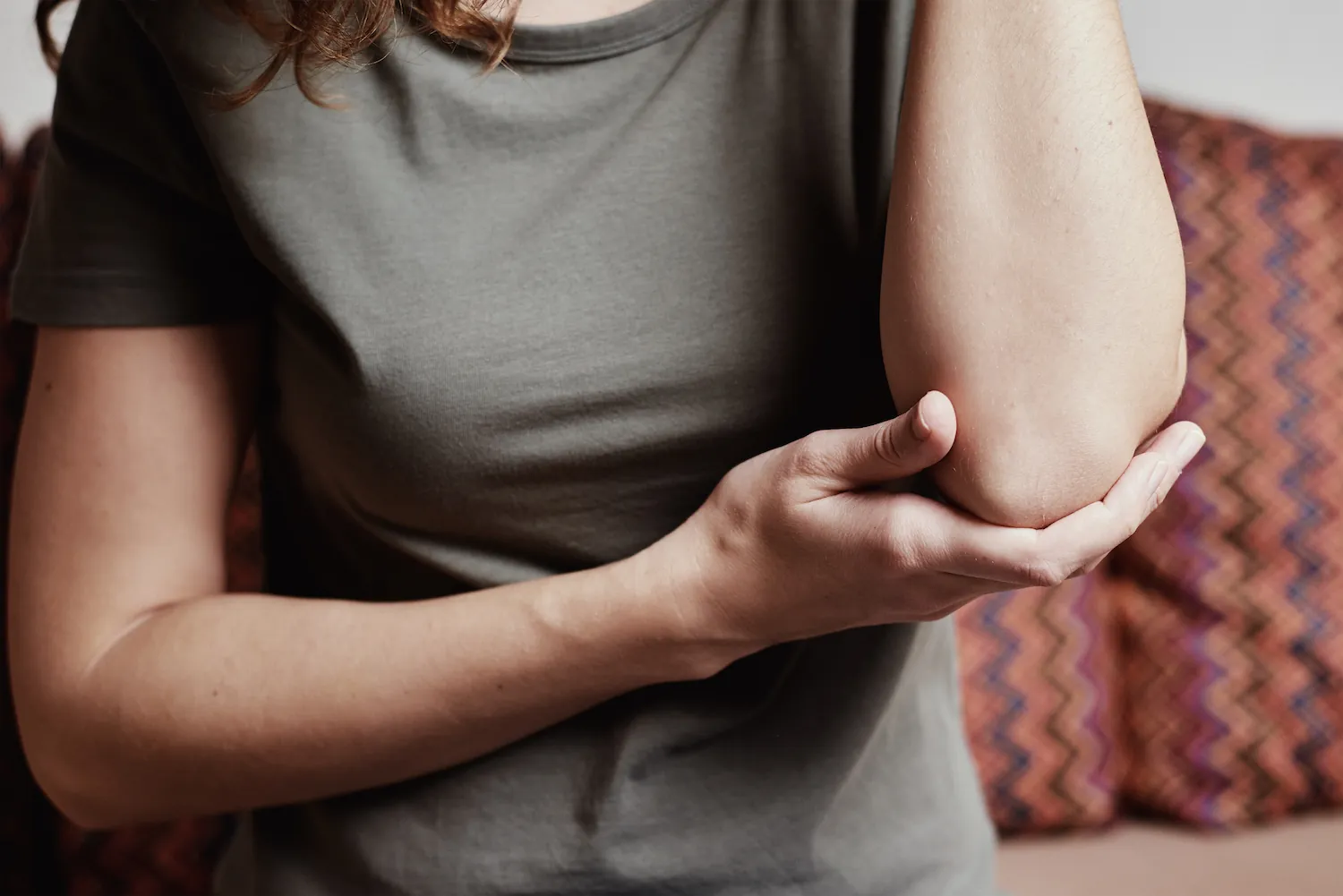 Woman in a gray shirt gripping her elbow