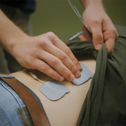 Hands placing electrical stimulation pads on a patient's back