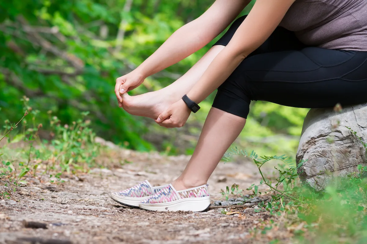 Woman sitting on a log holding her foot on a trail