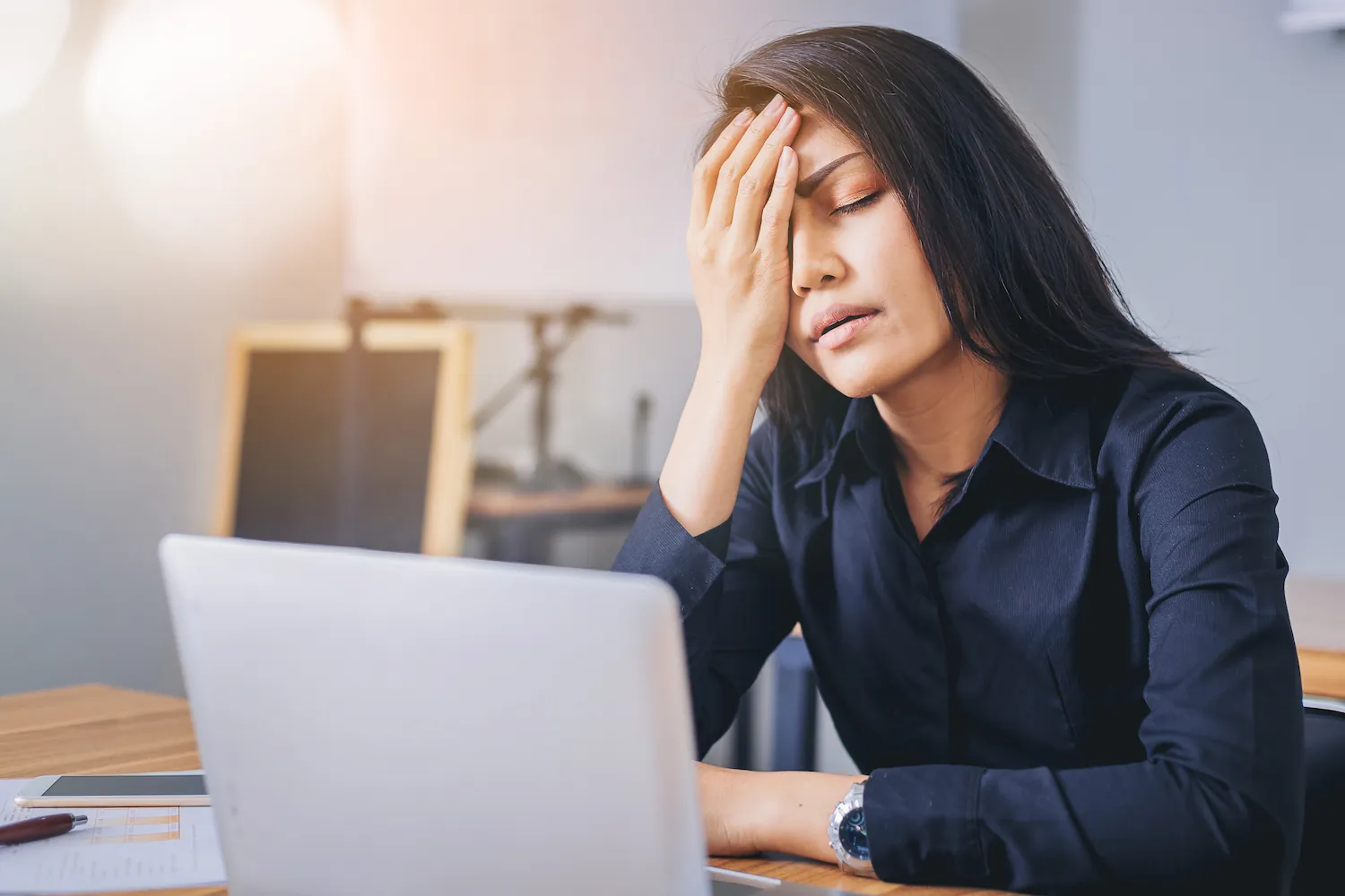Woman at a laptop with her hand on her forehead