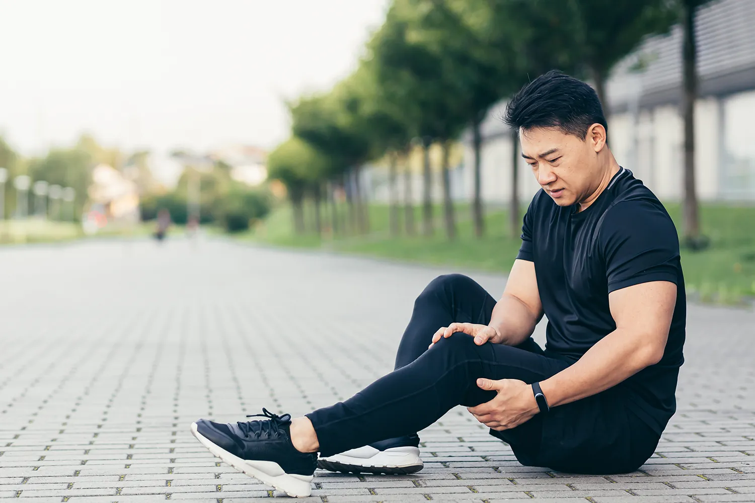 Man sitting on a paved path holding his leg after running