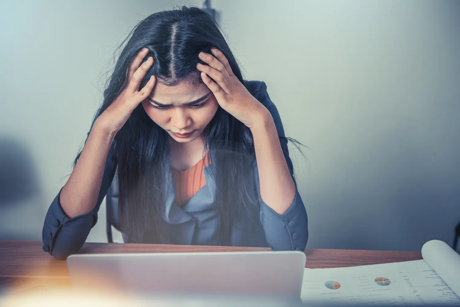 Woman at a desk looking down with both hands on her head