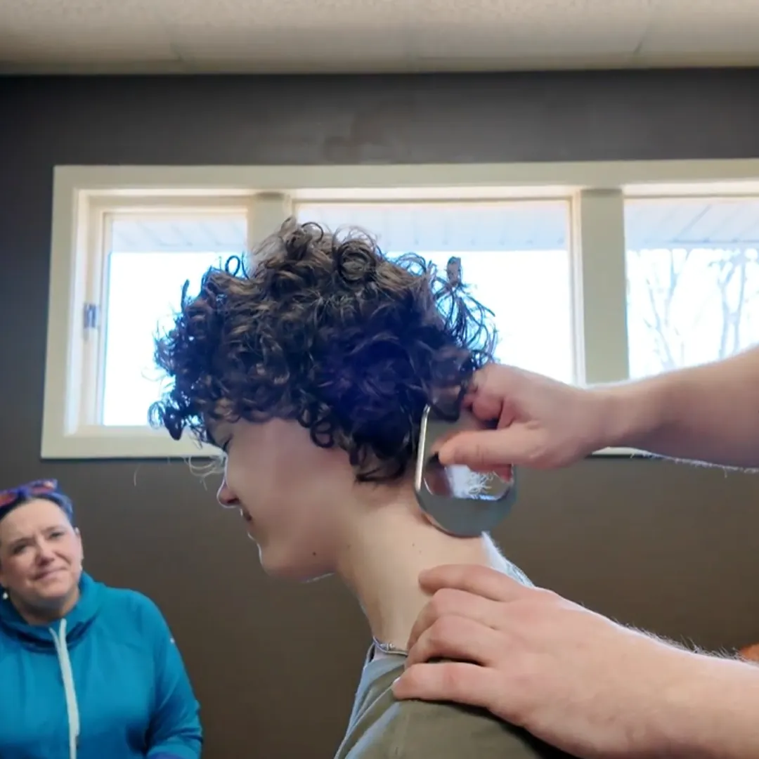 Practitioner using a scraping tool on a teen's neck