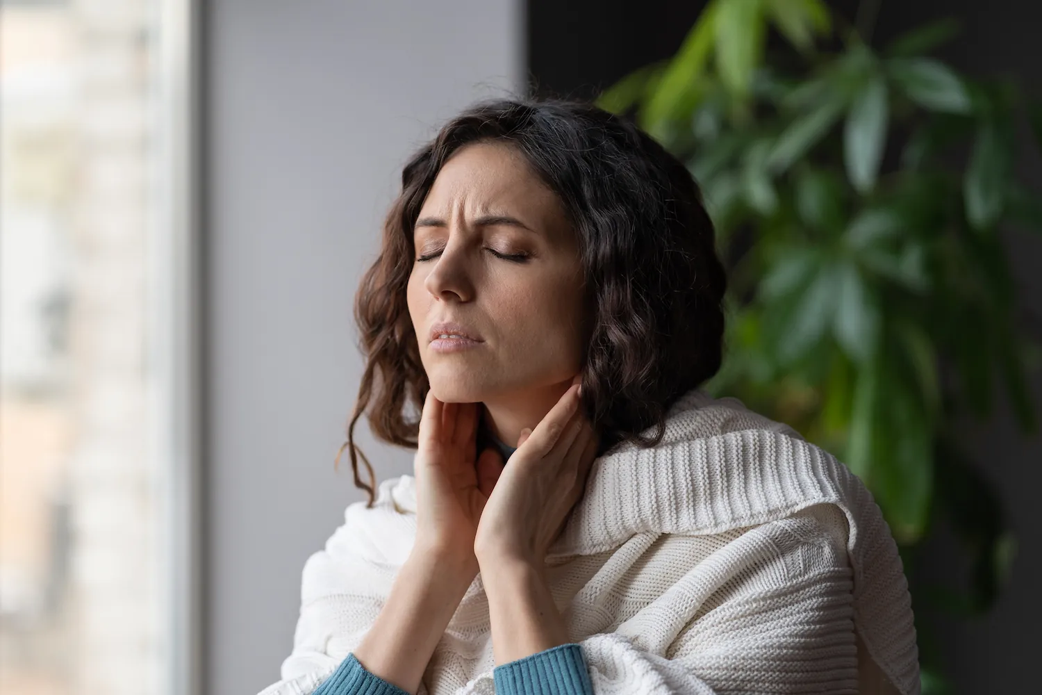 Woman holding her neck with eyes closed in discomfort