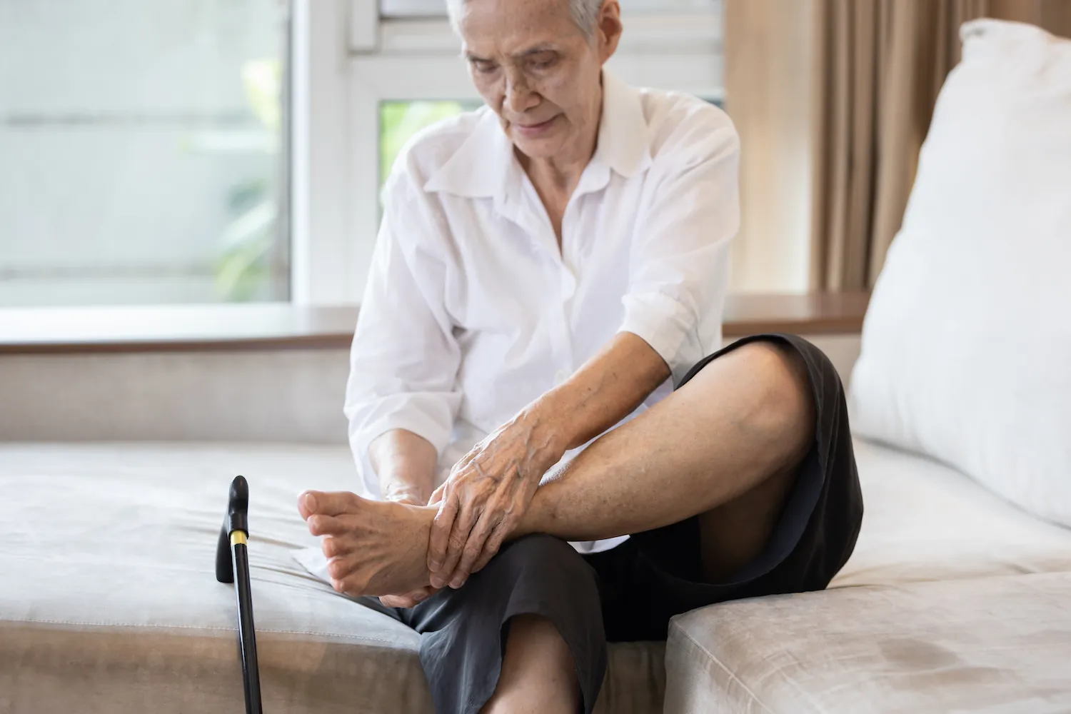 Older woman with a cane holding her foot on a couch