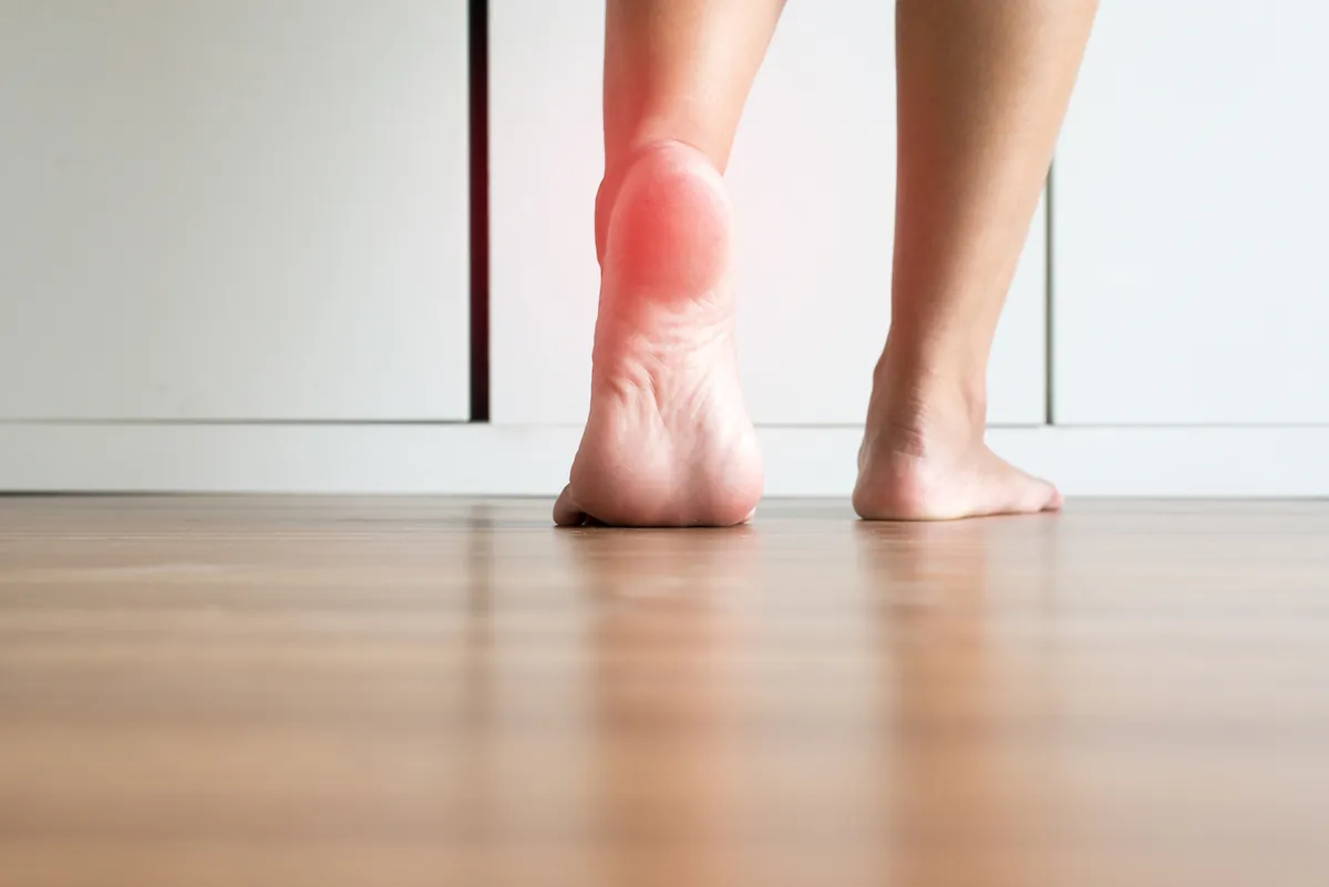 Bare heel highlighted red as a person stands on a wood floor