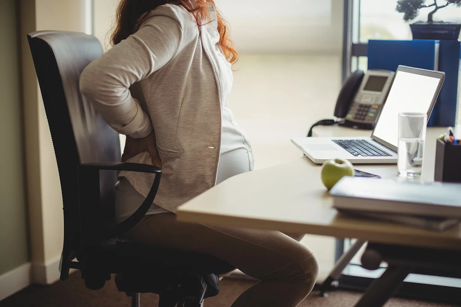 Pregnant woman at an office desk with a hand on her back
