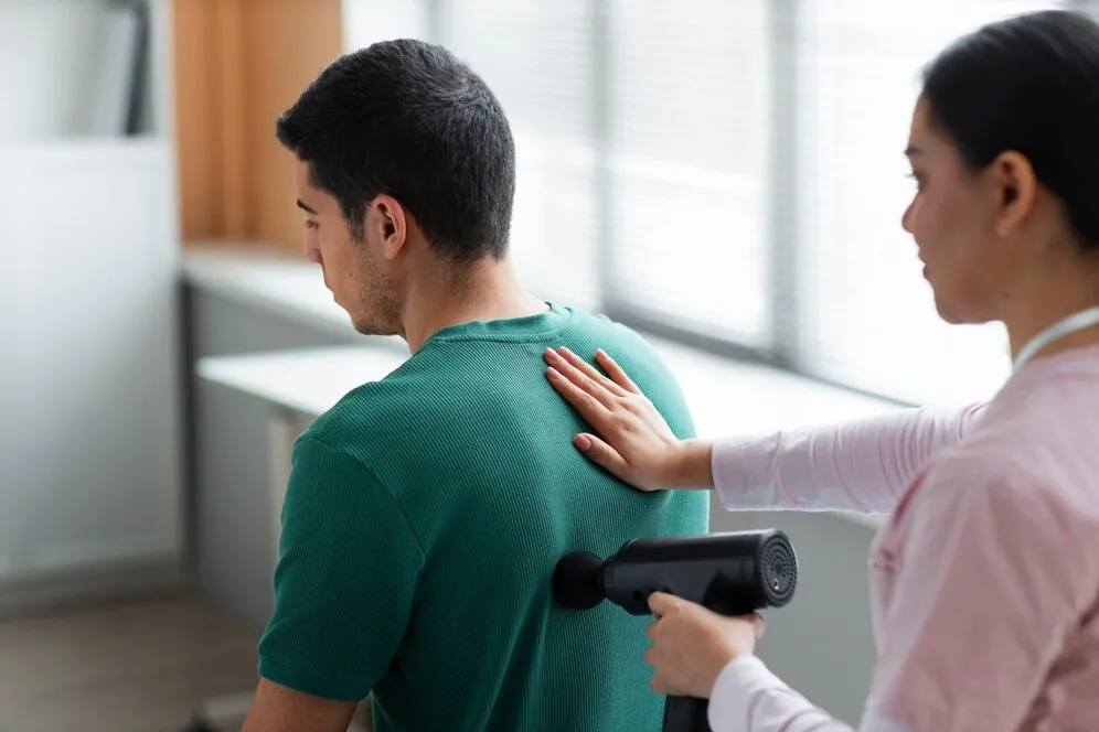 Therapist using a massage gun on a man's upper back