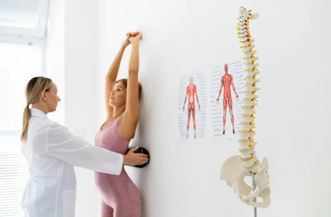 Doctor guiding a woman in a wall stretch beside a spine model