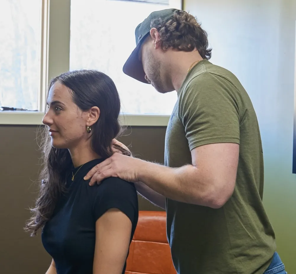 Chiropractor checking a woman's shoulder while she sits