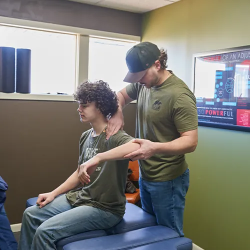 Chiropractor moving a seated patient's arm and shoulder