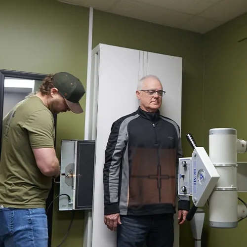 Patient standing at an x-ray unit with the chiropractor nearby